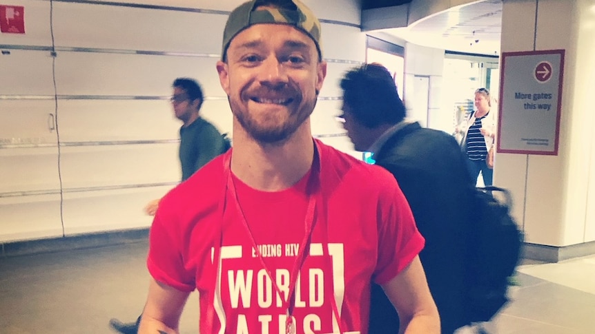 Man stands in red World Aids day top smiling 