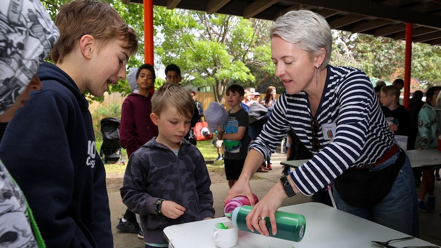 A woman hands out snow cones to children in re-usable cups instead of paper cones.