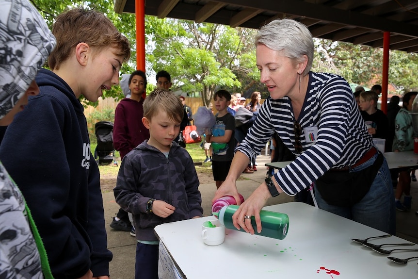 A woman hands out snow cones to children in re-usable cups instead of paper cones.