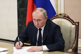 Russian President Vladimir putin sits at a table taking notes during a meeting of Russia's security council.