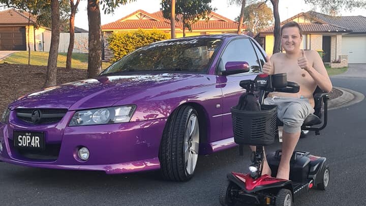 A young man on a mobility scooter, parked beside his purple Holden ute.