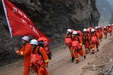 Chinese rescuers walk through hilly terrain.