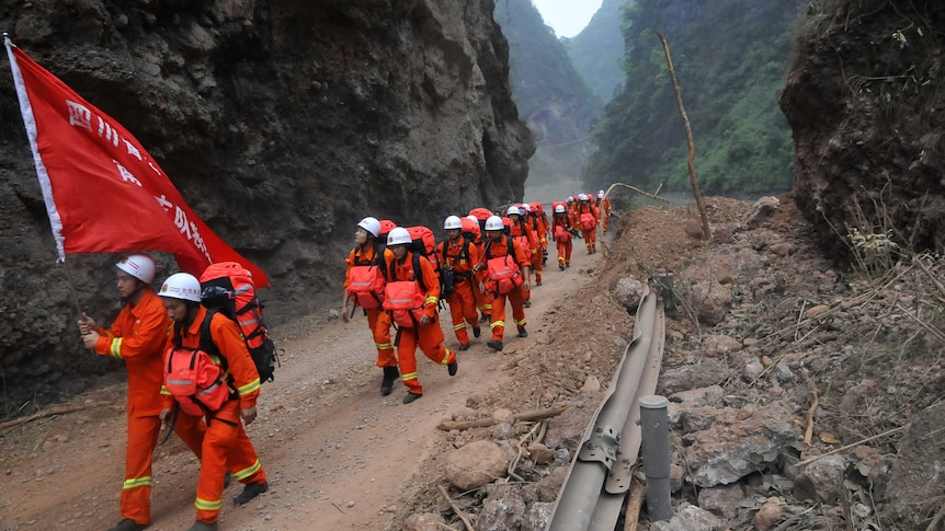 Chinese rescuers walk through hilly terrain.