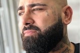 Close up portrait of man staring into distance, with tattoos on face and neck and beard.