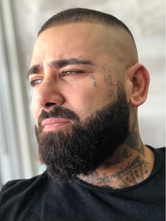 Close up portrait of man staring into distance, with tattoos on face and neck and beard.