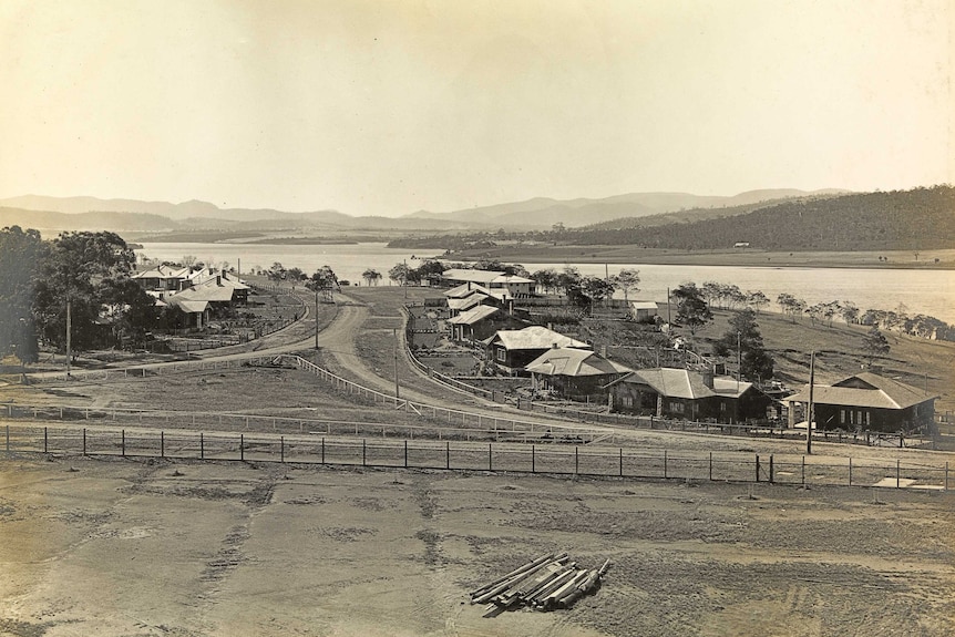 Sepia photo of a gravel road lined with wooden houses looking towards a river