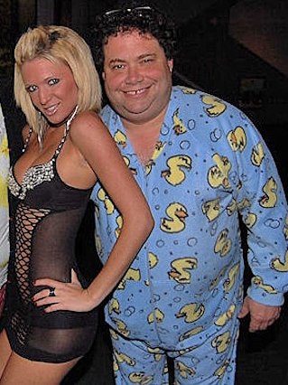 Blake Farenthold, wearing blue flannel pyjamas with yellow duckies on them, smiles broadly next to a blonde woman in lingerie.