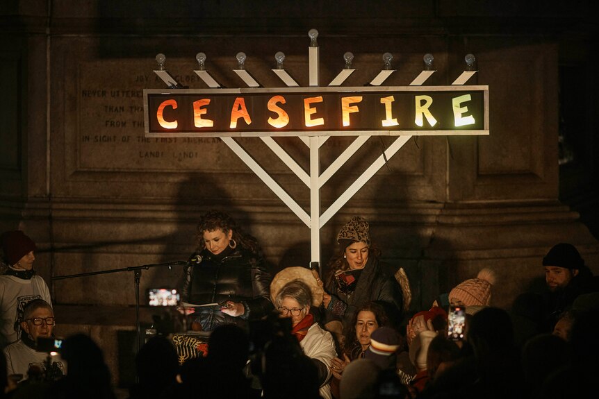 A group of people stand in front of a wall with "Ceasefire" written on it