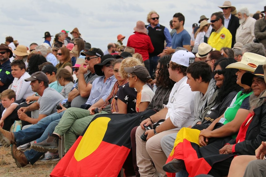 A crowd of people in all different coloured shirts, same wearing hats and others holding the Aboriginal flag