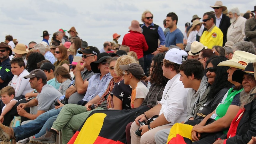 A crowd of people in all different coloured shirts, same wearing hats and others holding the Aboriginal flag