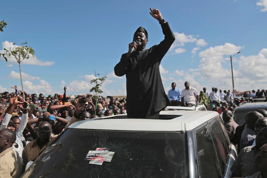 Opposition leader Raila Odinga speaks to a crowd from on top of a car.