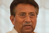 Pervez Musharraf stands at a lectern with microphones. He is wearing a gold ring on one finger.