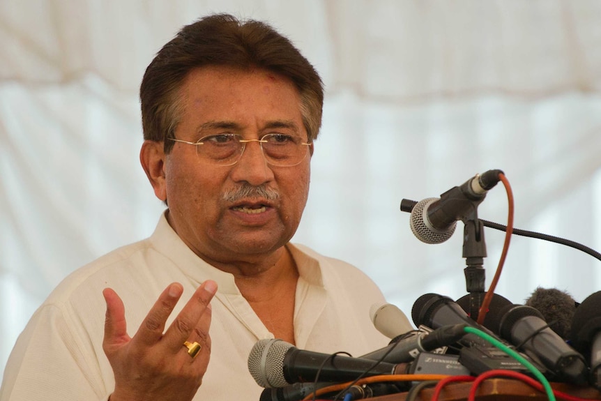 Pervez Musharraf stands at a lectern with microphones. He is wearing a gold ring on one finger.