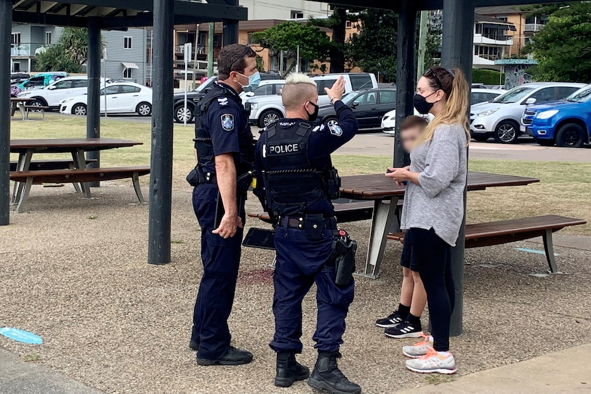 A pair of Queensland police speak to a woman in a park.