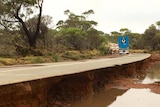 A long stretch of road that has been heavily damaged by flood water.