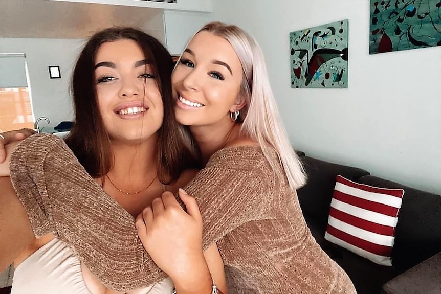 A girl with dark hair and a girl with blonde hair hugging and smiling at the camera.