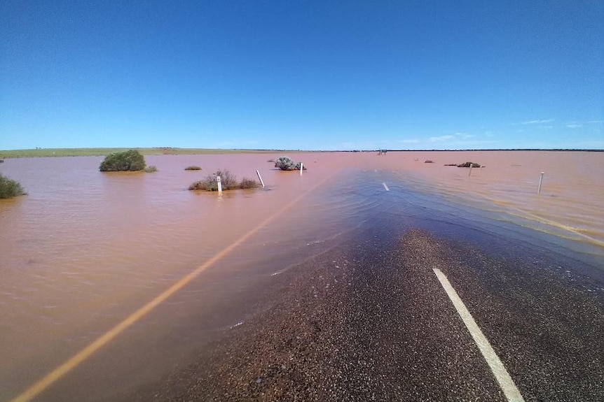 Flat straight road covered by red muddy water under a brilliant blue sky.