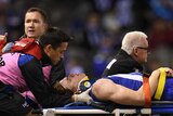 An AFL player in a neck brace lies on a stretcher with eyes closed as he is attended to.