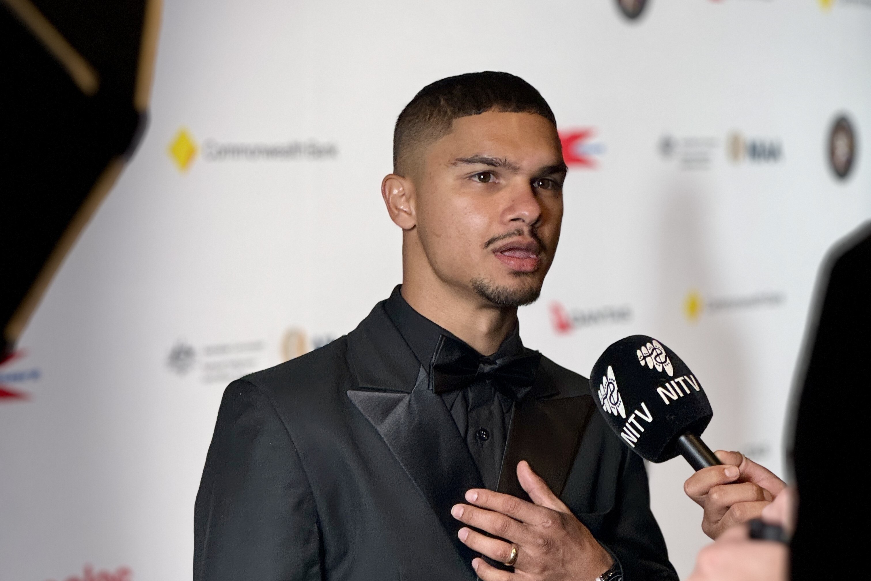 Man in black suit speaking to reporter holding a microphone
