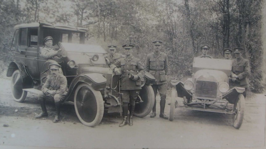 A black and white photo of eight men in Red Cross uniforms, standing around two cars during World War One.