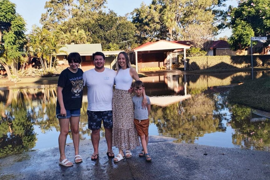 A family of four standing arm in arm in front of floodwaters.