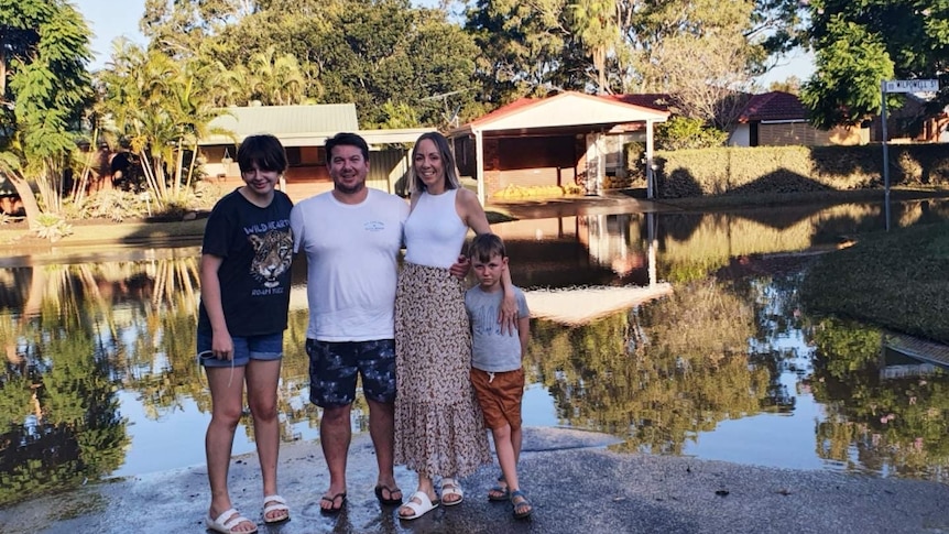 A family of four standing arm in arm in front of floodwaters.