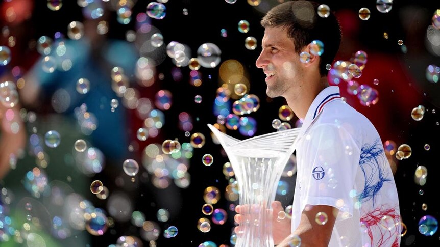 Novak Djokovic holds the winner's trophy and watches the bubbles after winning in Key Biscayne.