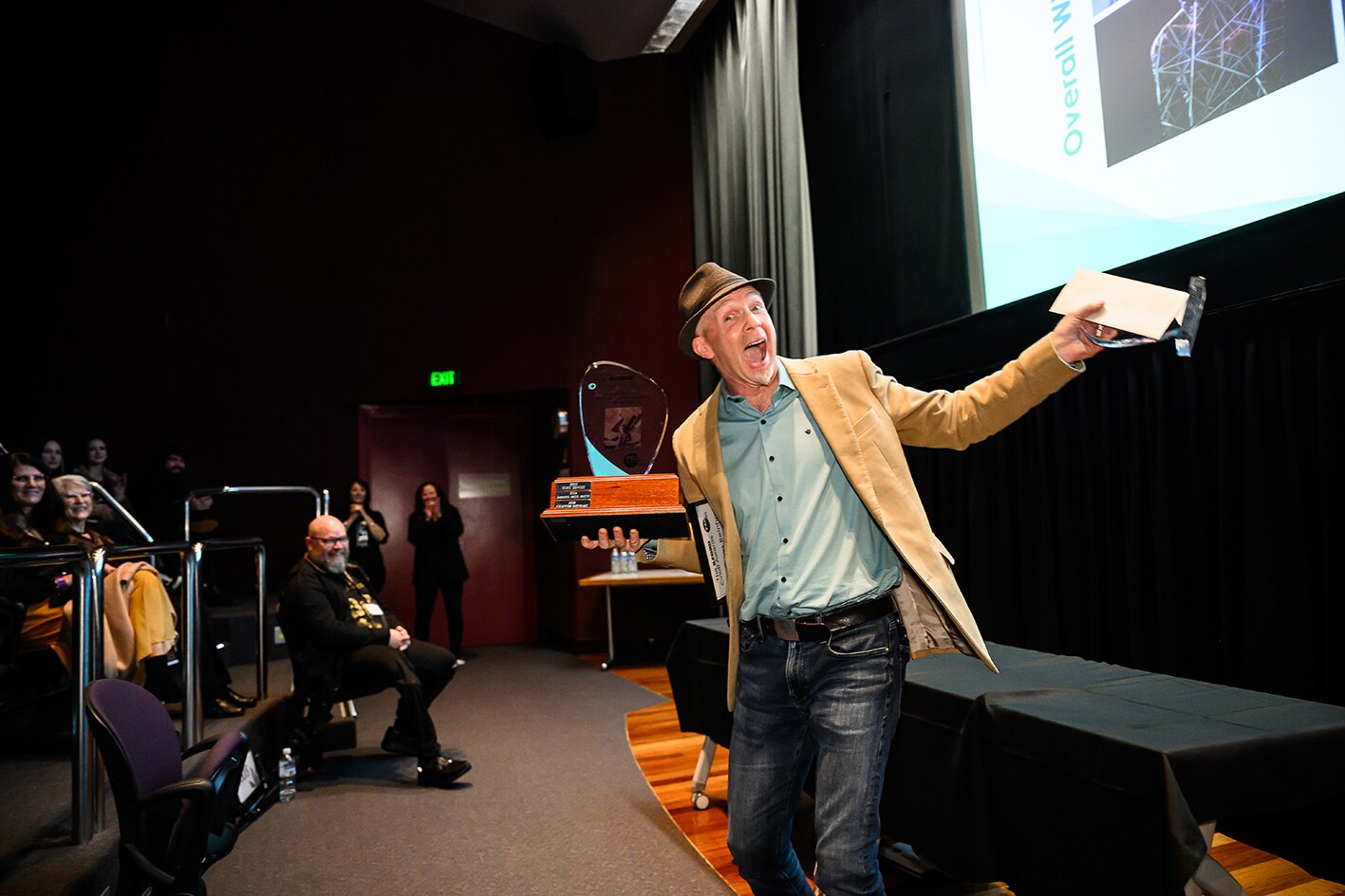 Man at front of auditorium holding trophy and smiling.