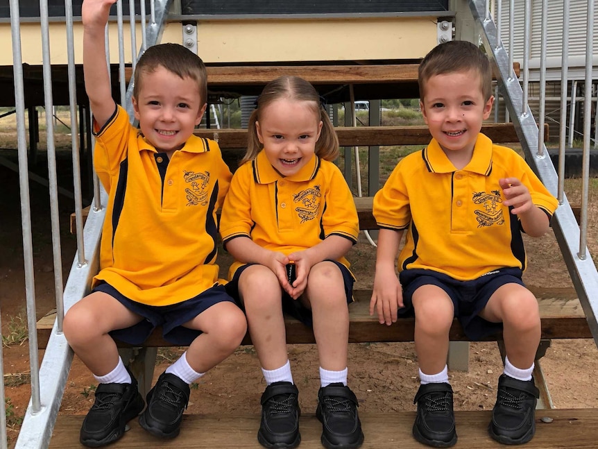 Three kindy students sit on the steps of a classroom.