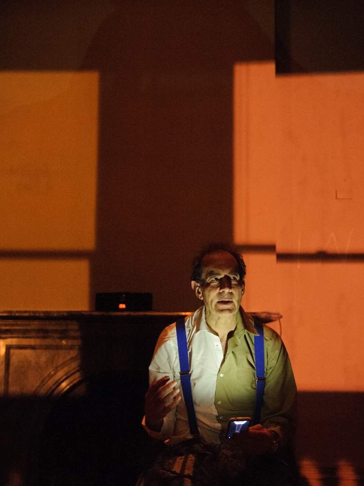 An actor, whose face is lit with white light, appears on a dimly-lit stage in the play Edmund: The Beginning.