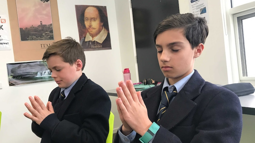 Two Boys clasp their hands together is if they are praying in their classroom