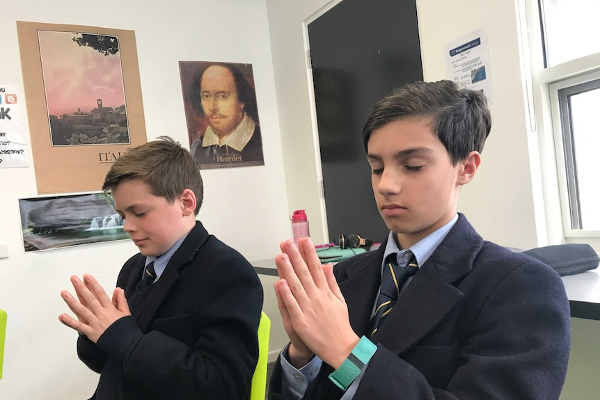 Two Boys clasp their hands together is if they are praying in their classroom