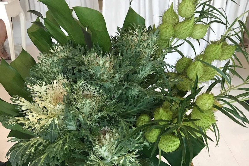 A floral arrangement containing cotton bush in front of white curtains.