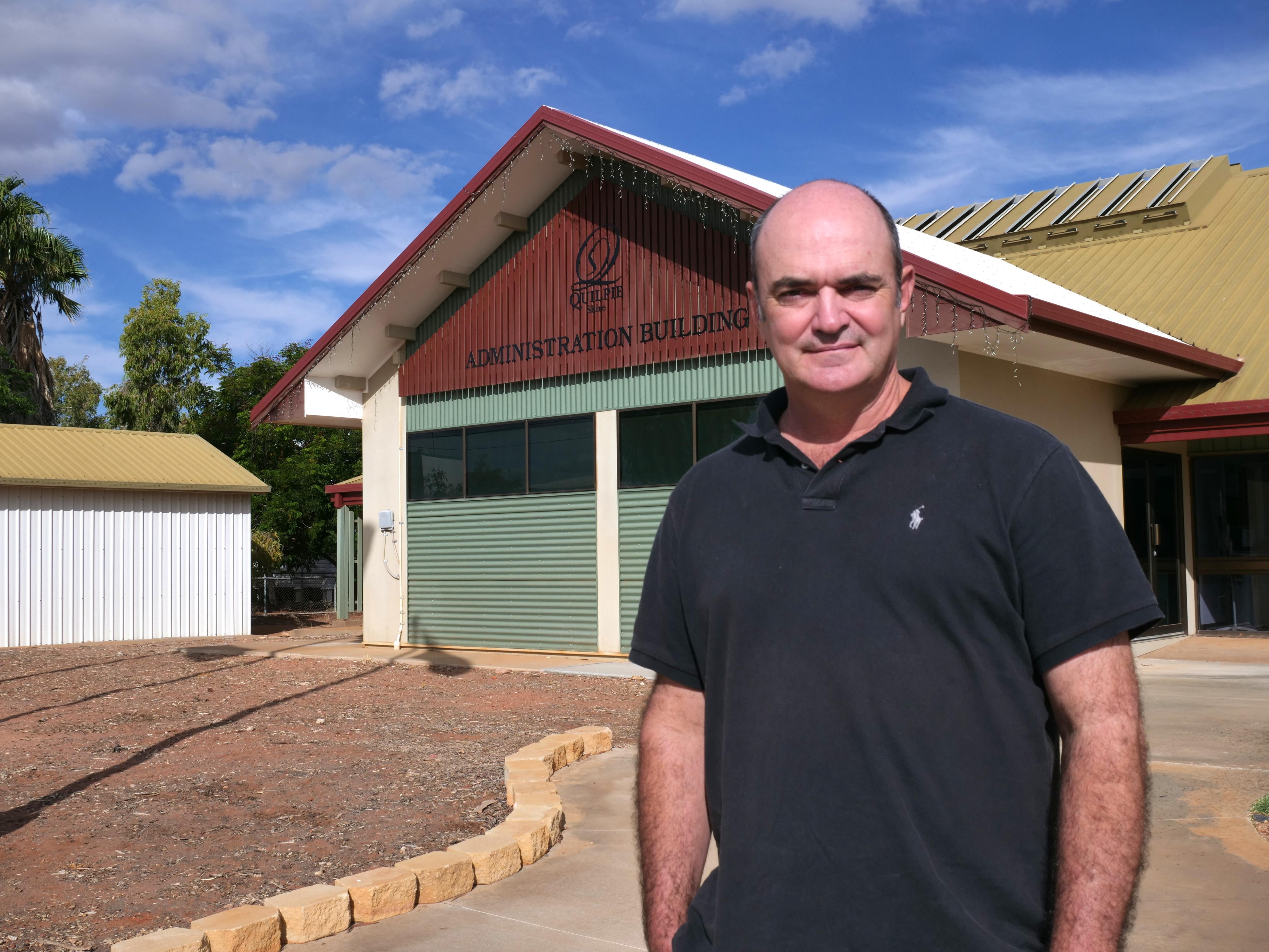 Bald man in black shirt stands out front of council building