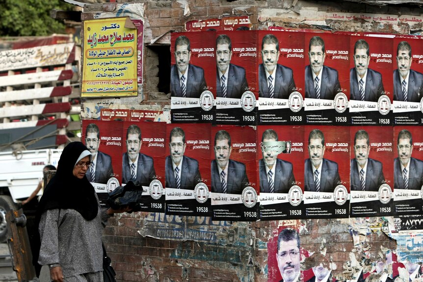 A woman walks past posters for Mohammed Mursi, who won the highest share of votes.