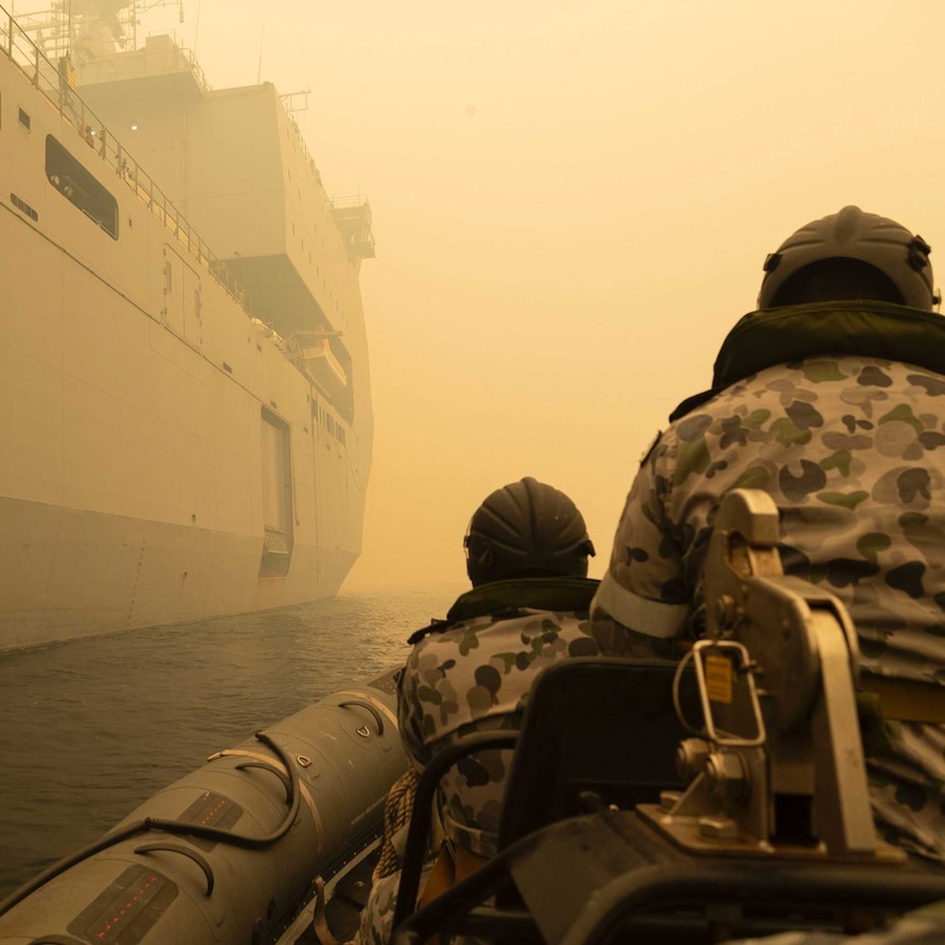The backs of two navy personnel on a boat through thick yellow smoke.