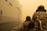 The backs of two navy personnel on a boat through thick yellow smoke.