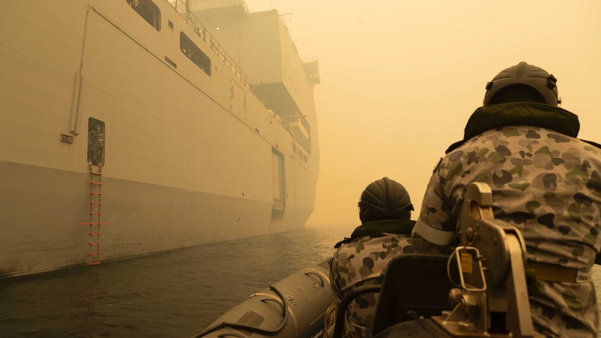 The backs of two navy personnel on a boat through thick yellow smoke.