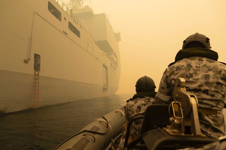 The backs of two navy personnel on a boat through thick yellow smoke.