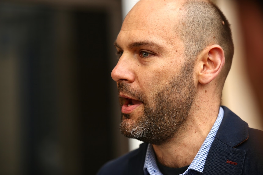 A man with a closely shaved head and a beard speaks outside of WA Parliament. A side on profile shot.