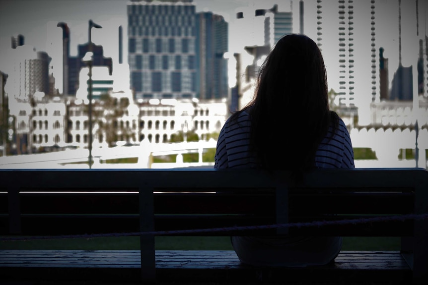 A woman sitting on a park bench shot from behind