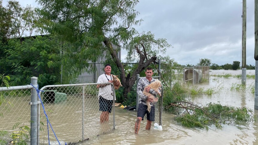 Two men carry dogs through floodwater