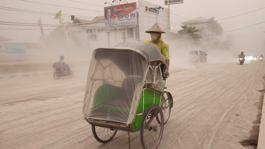 Man riding becak through ash from Indonesian volcano