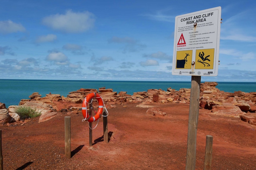 A life ring and warning sign on a red dirt outcrop above the sea