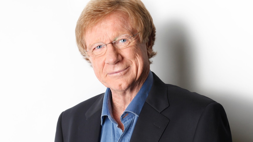 Journalist Kerry O'Brien standing against white wall.