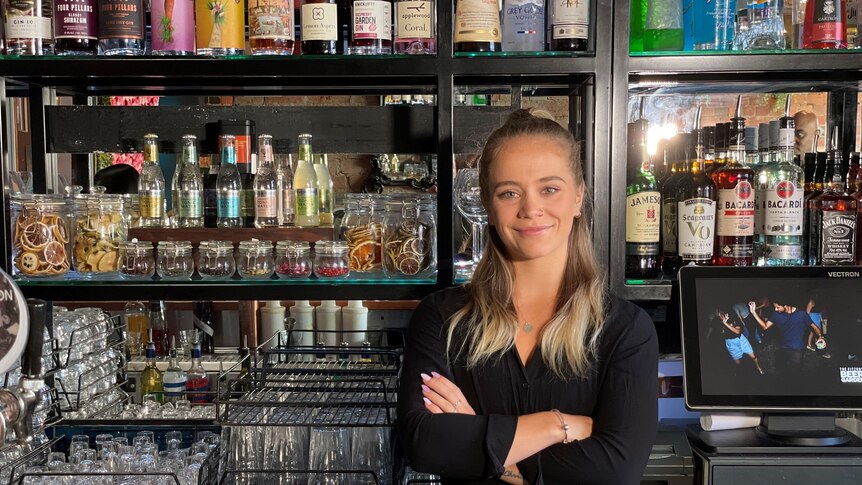 A woman with her arms folded standing behind a bar.