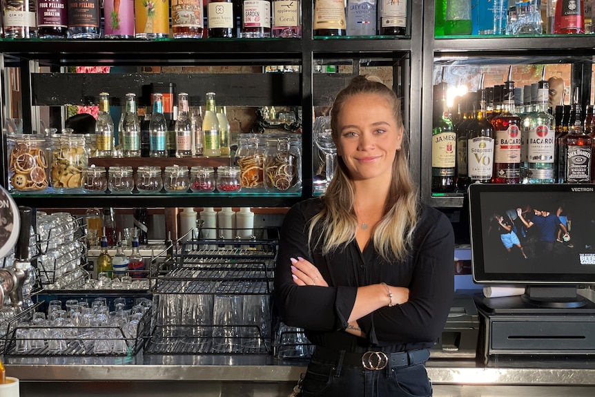 A woman with her arms folded standing behind a bar.