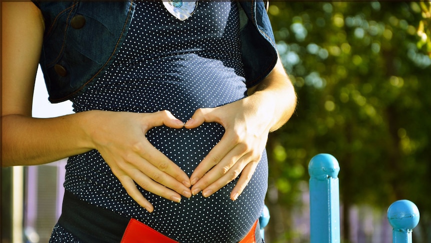 A pregnant woman holds her hands to her belly.