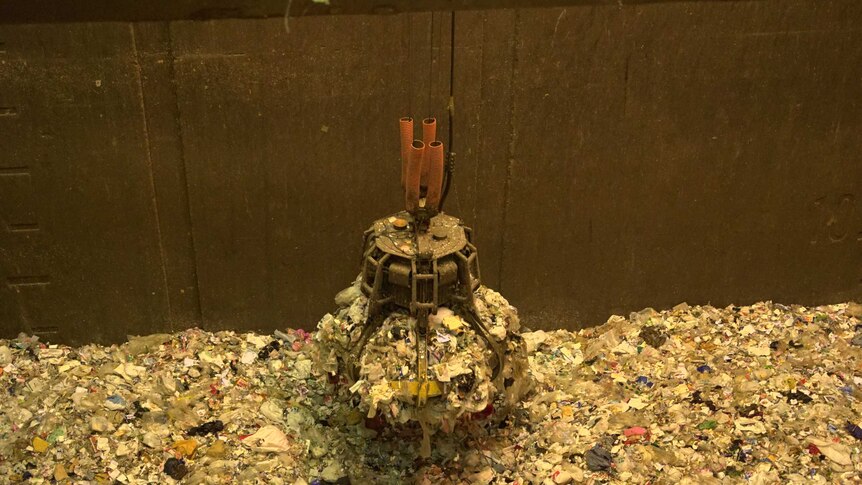 A crane collects a large amount of rubbish from a pile