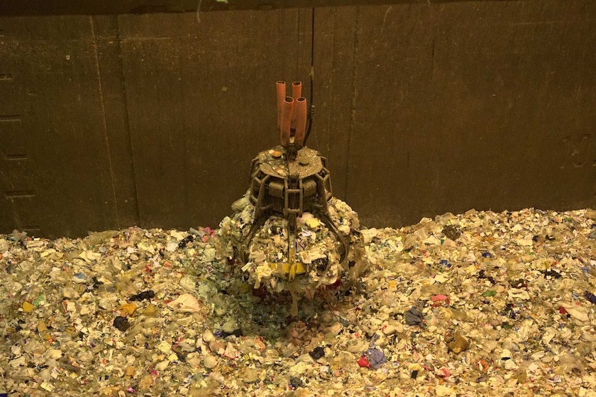 A crane collects a large amount of rubbish from a pile